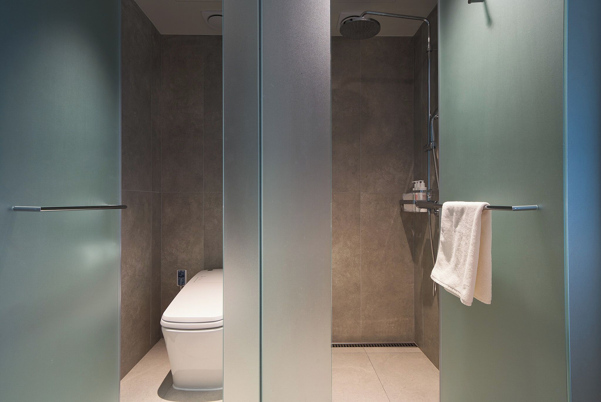 A modern bathroom with a glass partition, a toilet, a shower area, and a towel rack.