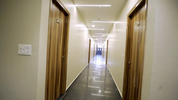 A long, narrow hallway with wooden doors on either side, leading to a bright room at the end.