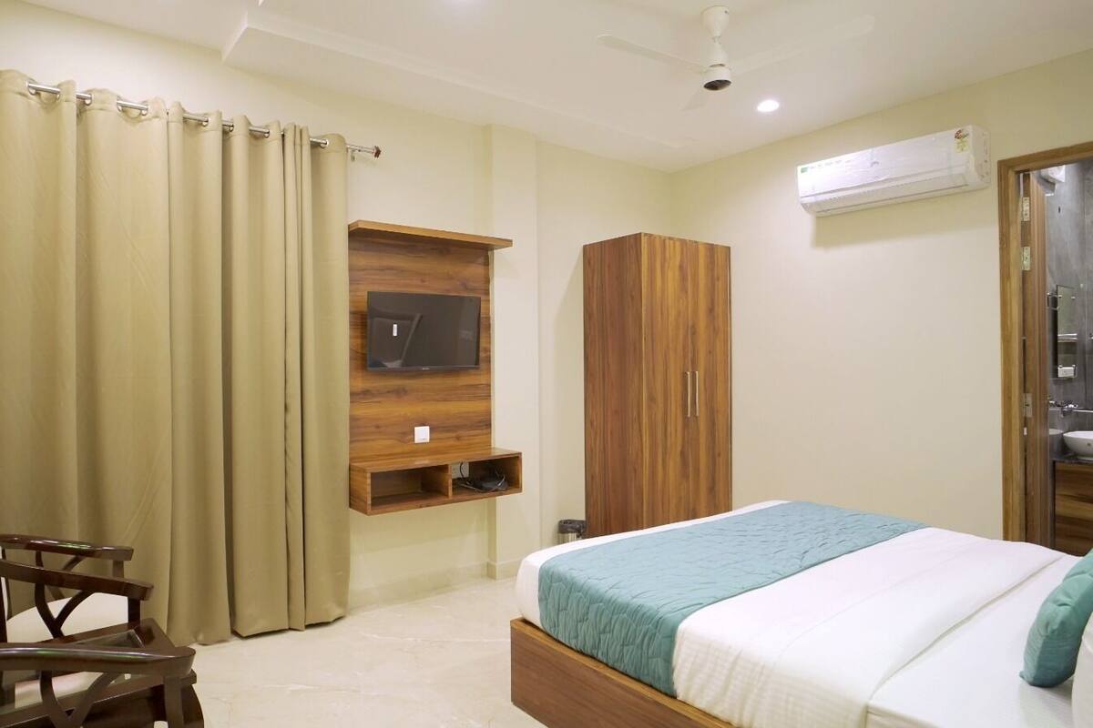 Habitación de hotel con cama, televisión montada en la pared, armario y baño visible a través de una puerta abierta.