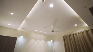 Una habitación con ventilador de techo, luces empotradas y una cortina.