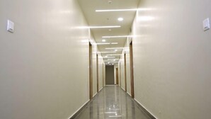 Un pasillo largo y estrecho con piso negro brillante y paredes blancas. Hay varias luminarias en el techo, y el pasillo parece estar bien iluminado.