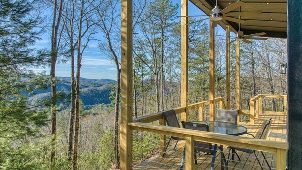 Una terraza de madera con una mesa y sillas, rodeada de árboles y un paisaje montañoso.