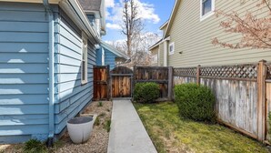 A residential property with a narrow pathway leading to a wooden gate, surrounded by a wooden fence and a small bush. - DOG FRIENDLY & EPIC Location! Walk 2 Blocks to Hyde Park | Cozy Up by the Fireplace! (Boise)