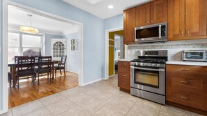 A kitchen with wooden cabinets, stainless steel appliances, and a dining area with a table and chairs. - DOG FRIENDLY & EPIC Location! Walk 2 Blocks to Hyde Park | Cozy Up by the Fireplace! (Boise)