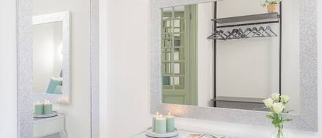 Un baño con un espejo grande, una tocador con una revista, dos velas y un florero con flores.