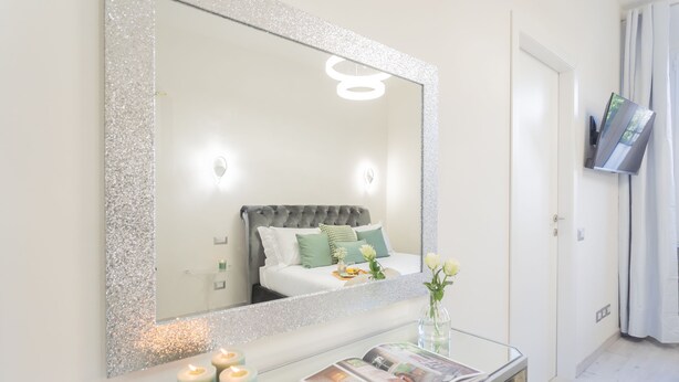 Un dormitorio con un espejo grande, una mesita de noche con velas y una cama con almohadas verdes.