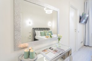 A bedroom with a large mirror, a bedside table with candles, and a bed with green pillows. - Cernobbio Green Suite (Cernobbio)