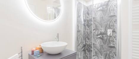 A modern bathroom with a white sink, round mirror, and glass shower enclosure with a leaf pattern.
