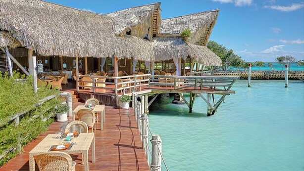 An overwater bungalows with thatched roofs, wooden deck seating, and a view of the turquoise sea.