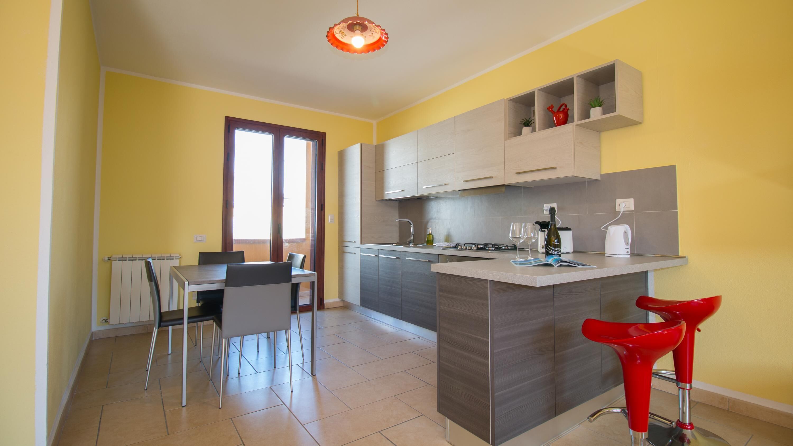 A modern kitchen with a dining area, featuring a central island with bar stools, a built-in oven, and a window with curtains.