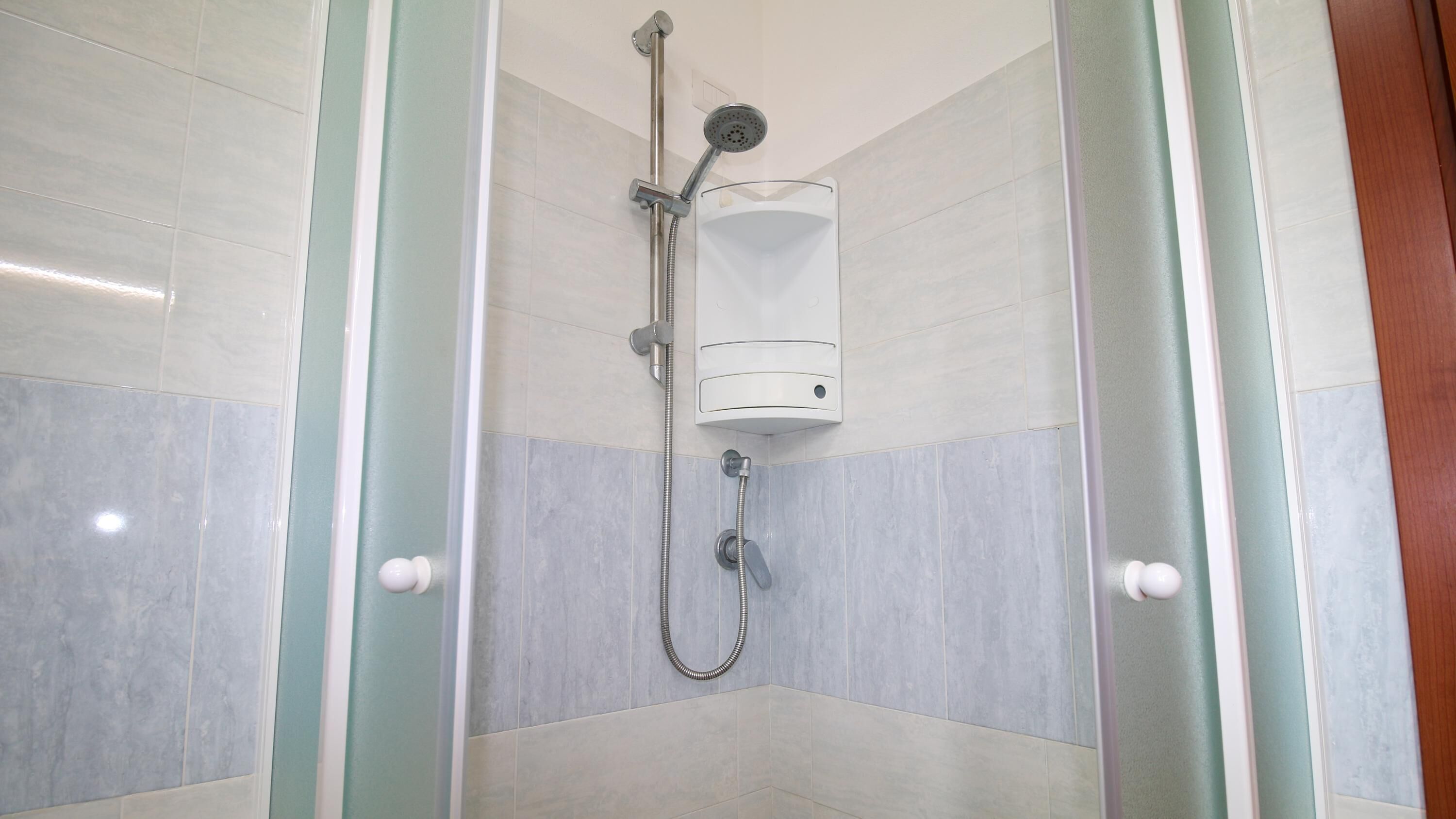 Ducha con mampara de vidrio, cabezal de ducha manual y panel de control en la pared.