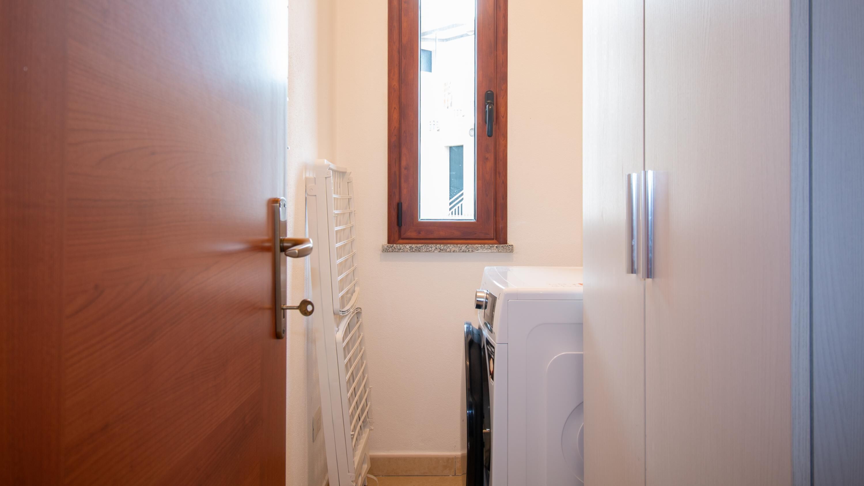 A narrow hallway with a wooden door on the left, a white radiator, and a window with a wooden frame.