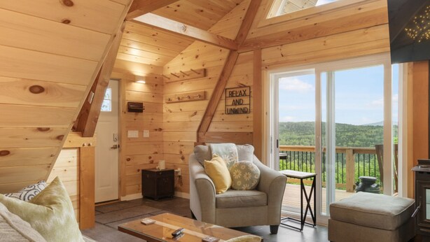 Una cabaña de madera acogedora con un dormitorio en el entrepiso, una sala de estar con sofá y sillones, y un balcón con vistas panorámicas.