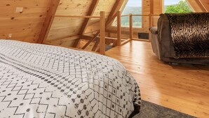 Una habitación con techo alto de madera, con cama, sofá y vistas al exterior.