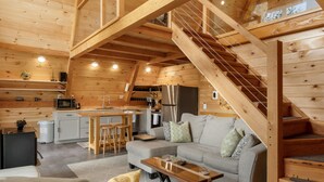 Interior espacioso de una cabaña de madera con cocina, comedor y una escalera que conduce a un nivel superior.