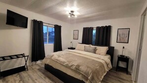 A bedroom with a bed, a TV, a ceiling fan, and a window with curtains.