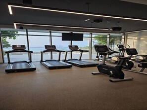 Une salle de sport équipée de tapis de course, d’un vélo elliptique et d’un vélo d’appartement, avec de grandes fenêtres donnant sur un plan d’eau.