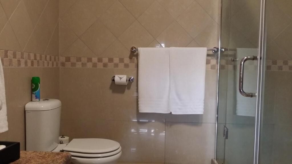 A bathroom with a toilet, a glass shower enclosure, a towel rack with two towels, and a toilet paper holder.