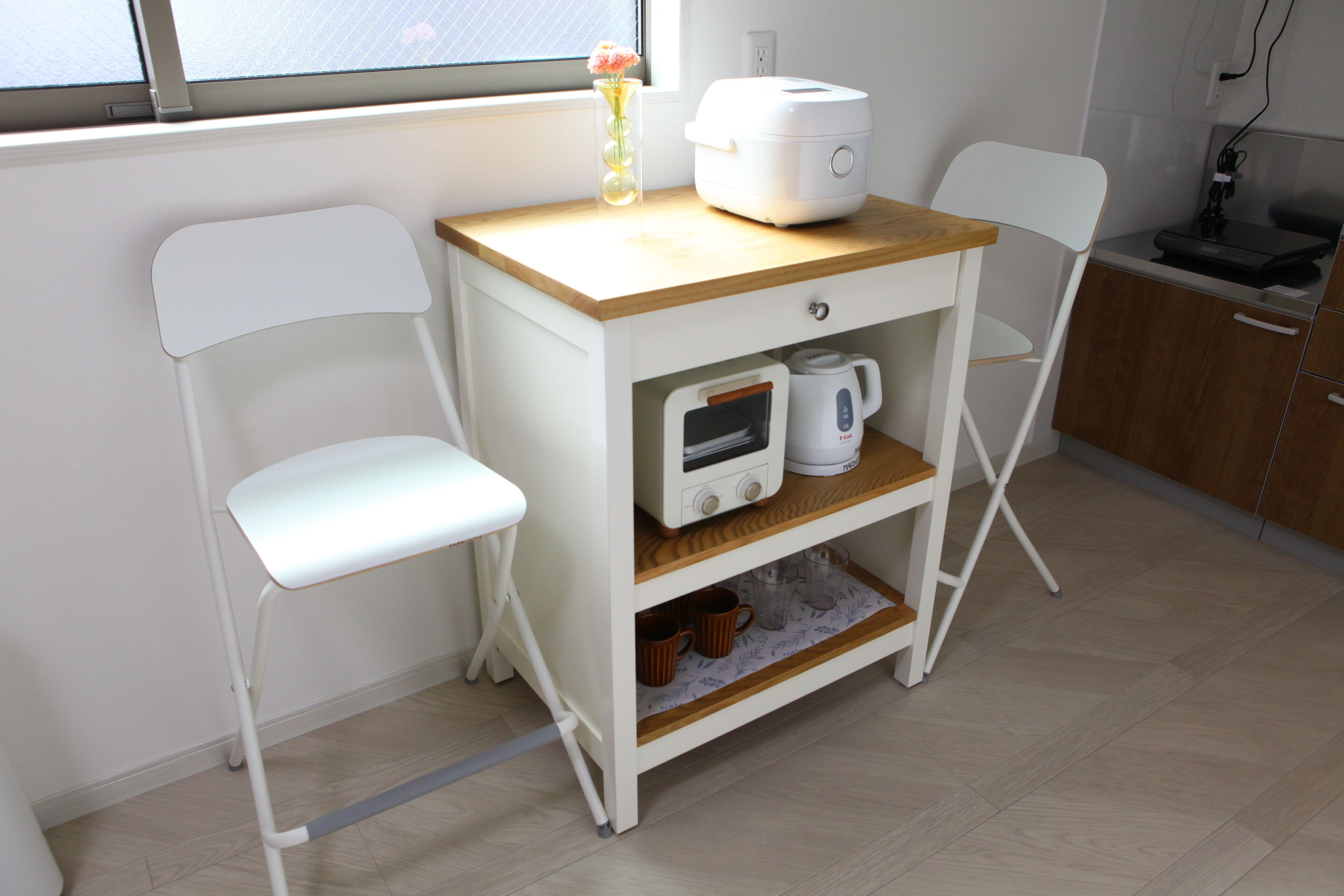 Cuina compacta amb taulell blanc, cafetera i cadira blanca.