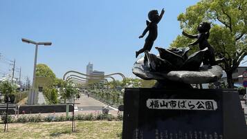 A park with a statue of a child on a rock, surrounded by flowers and a clear sky.