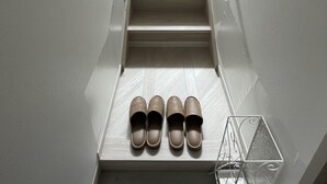 Eine Treppe mit Geländer auf der rechten Seite, die zu einer Zwischenebene führt, wo vier Paare brauner Hausschuhe auf einem Regal liegen.