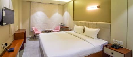 A hotel room with a large bed, a desk with a chair, a small table, a TV mounted on the wall, and a ceiling fan.