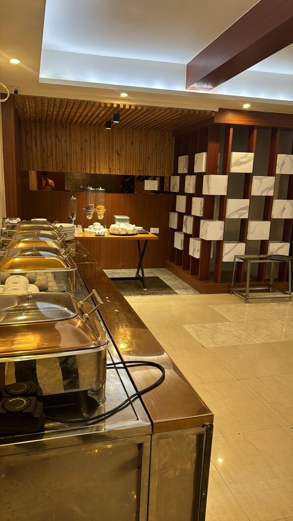 A buffet area with multiple serving stations, a wooden wall with a patterned design, and a tiled floor. - The Urban Villa (Varanasi)
