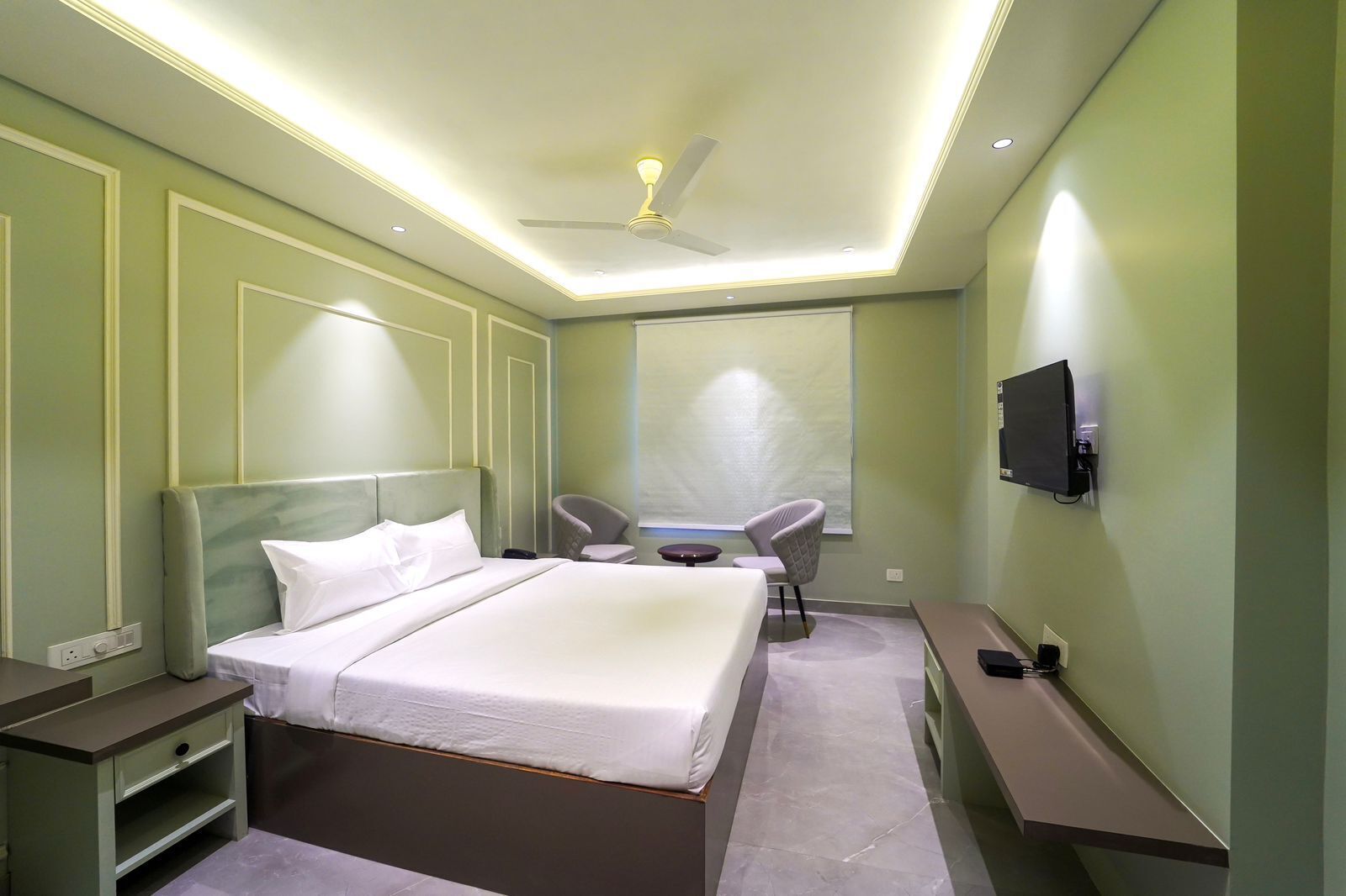 Une chambre d’hôtel moderne équipée d’un grand lit, d’un bureau, de deux chaises, d’une télévision et d’un ventilateur de plafond.