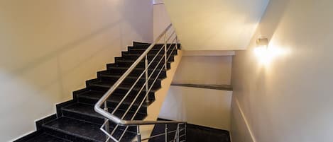 A modern staircase with black marble steps and metal railings, leading to a landing with a handrail.