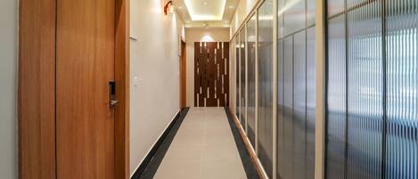 A hallway with wooden doors, a tiled floor, and a glass partition on one side.