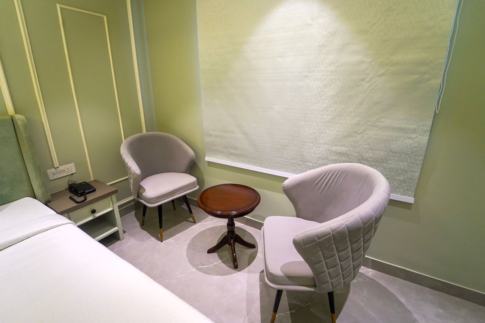 A small, private room with two white armchairs, a small round table, and a bed.