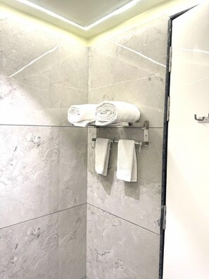 Un baño con cabina de ducha de vidrio, paredes de mármol y un perchero con toallas dobladas.