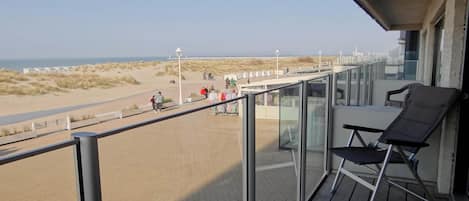En balkon med udsigt over stranden, en stol og et gelænder.