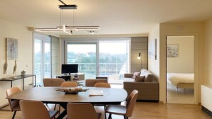 A modern living room with a dining area, large windows, and a view of the outdoors. - Apartment in Nieuwpoort near the Beach (Nieuwpoort)