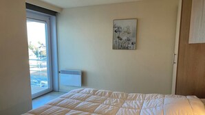A bedroom with a large bed, a window with a view of the outside, a wall-mounted air conditioner, and a painting on the wall. - Apartment in Nieuwpoort near the Beach (Nieuwpoort)