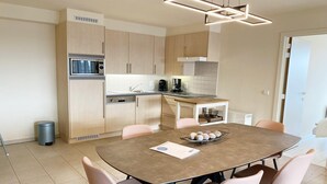 A modern kitchen with a microwave, coffee maker, and a dining area with a round table and chairs. - Apartment in Nieuwpoort near the Beach (Nieuwpoort)