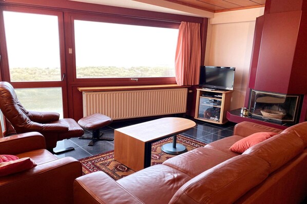 A living room with leather sofas, a coffee table, a TV, and a fireplace. - Chic Urban Seaside Apartment (Nieuwpoort)