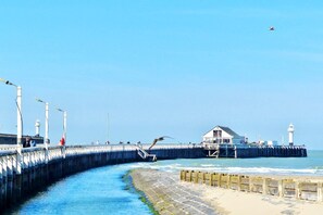 A coastal pier with a lighthouse, a wooden walkway, and a building with a sloped roof. - Chic Urban Seaside Apartment (Nieuwpoort)