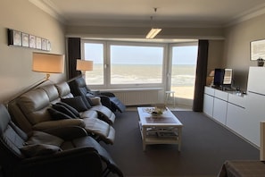 Habitación de hotel con sofá, mesa de centro, televisión y vista a la playa.