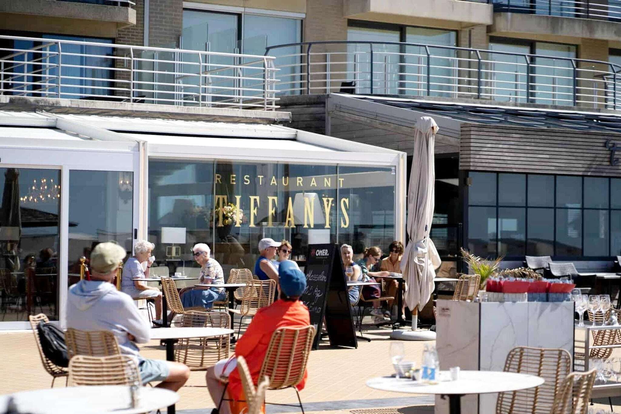 Un ristorante all'aperto con sedie e tavoli in vimini, facciata in vetro e un cartello con la scritta "RESTAURANT TIFANY'S".