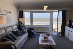 Habitación de hotel con sofá, mesa de centro, televisor y vista a la playa.