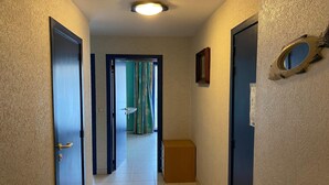Un couloir doté d’un sol carrelé, une porte avec une poignée, un petit meuble en bois et un miroir fixé au mur.