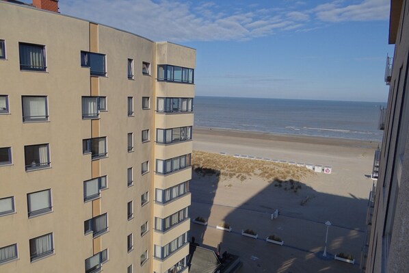 A high-rise building with multiple windows and balconies overlooking a beach.