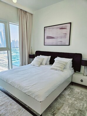 A modern bedroom with a large bed, a city view, and a minimalist abstract painting. - 2BRwith Panoramic Sea View in Beachfront (Dubai)