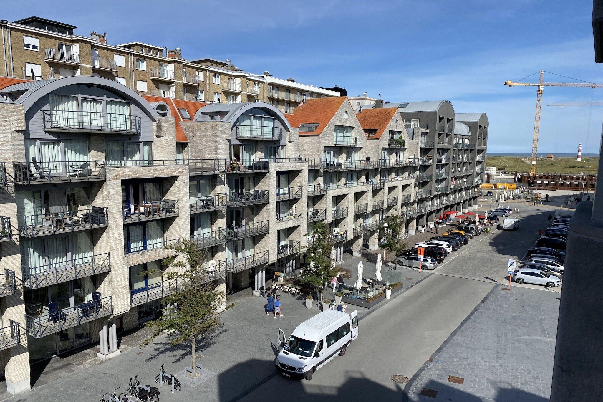 Ein mehrstöckiges Hotel mit Balkonen, einem Parkplatz und einem Baukran im Hintergrund.