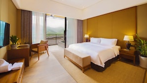 Habitación de hotel con una cama grande, un escritorio, una silla, un televisor, un balcón y vistas a las montañas.