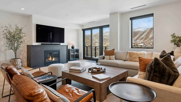 A modern living room with a fireplace, leather sofas, a coffee table, and large windows offering a mountain view. - Frontgate 302 - 5 Bedroom Residence (Avon)