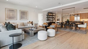 A modern living room with a sofa, coffee table, ottomans, and a dining area with chairs and a table. - Frontgate 302 - 5 Bedroom Residence (Avon)