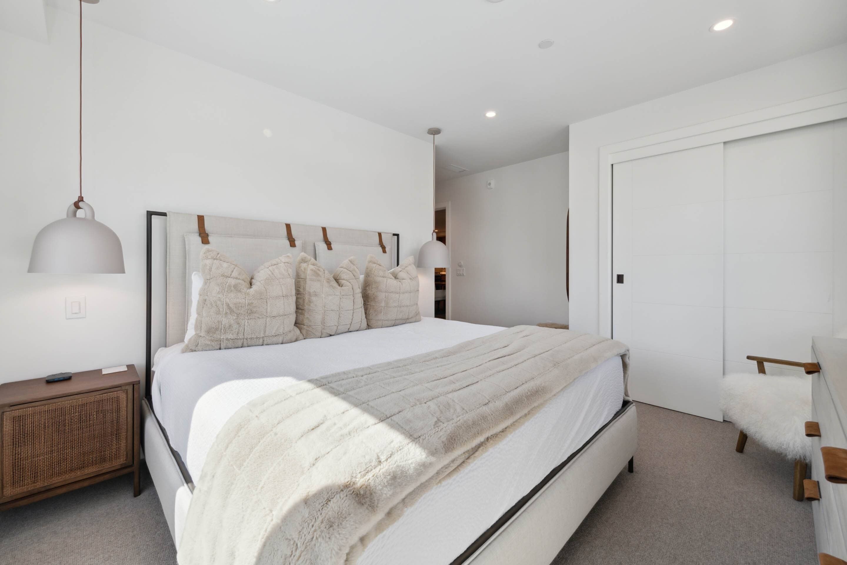 Une chambre à coucher moderne avec un grand lit, une table de chevet, une lampe et une armoire.