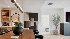 A modern dining area with a wooden table, black chairs, a large black vase with a plant, and a geometric wall art piece. - Frontgate 302 - 5 Bedroom Residence (Avon)